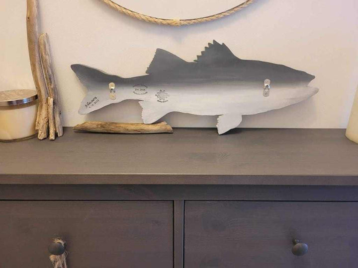 Hand-painted striped bass artwork displayed on a shelf with a natural decor theme.