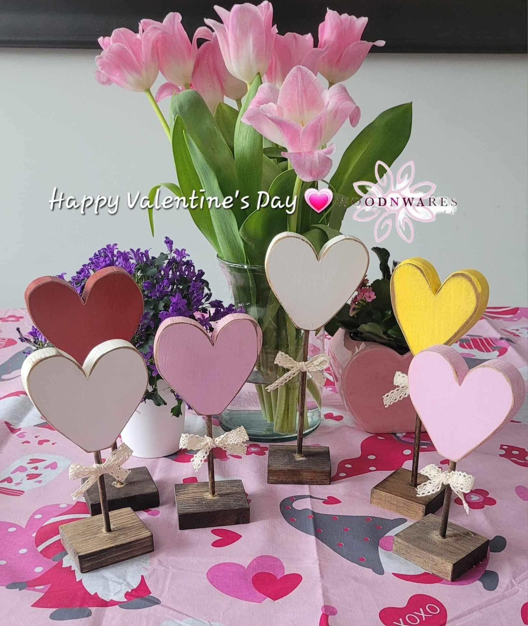Handcrafted wooden hearts with bows displayed on a Valentine's-themed table with pink flowers.