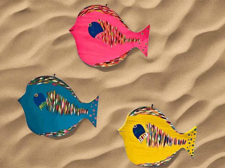 Colorful hand-painted folk art fish on sand background, showcasing vibrant and detailed designs.