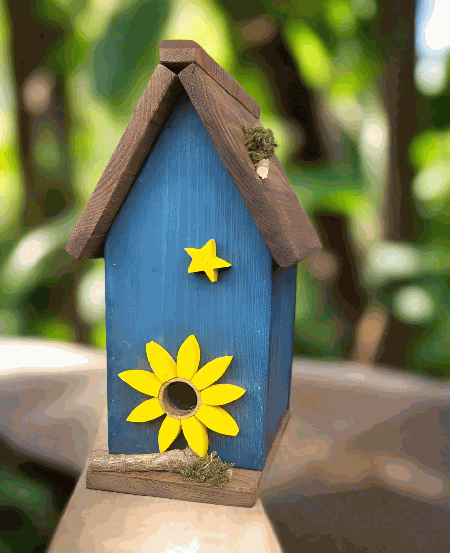 Handmade pine birdhouse with blue finish and decorative yellow flower and star.