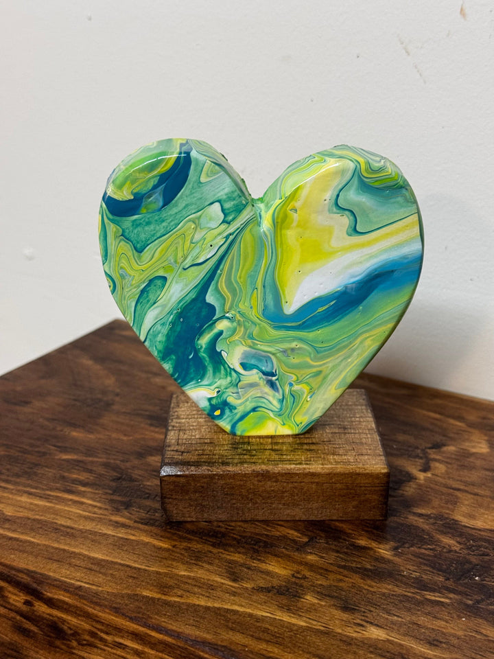 Heart-shaped sculpture with green and blue marbled design on a wooden stand against a white background