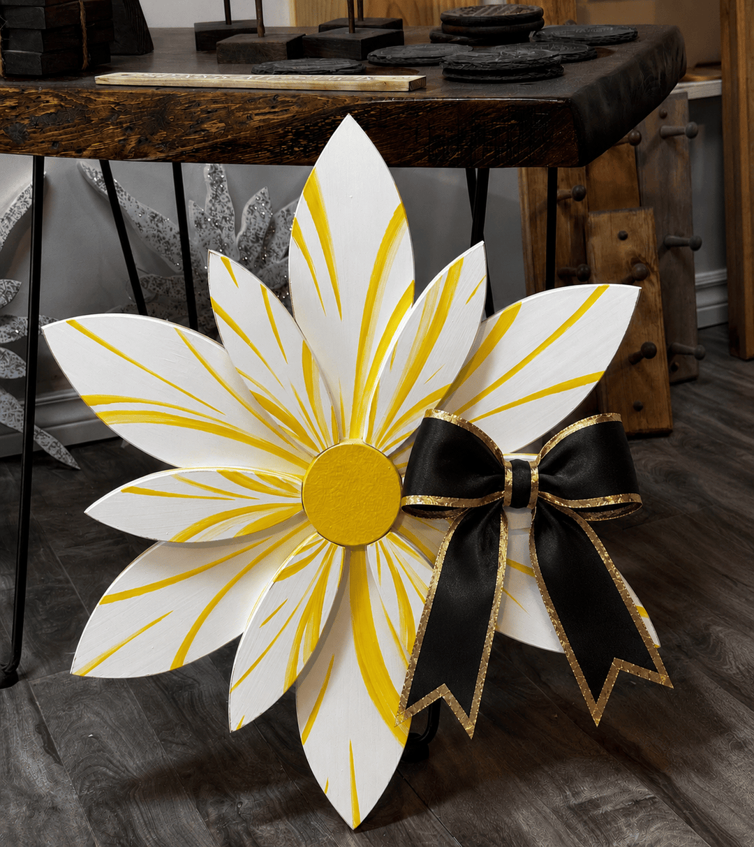 Decorative flower with yellow petals and a black bow on a wooden floor.