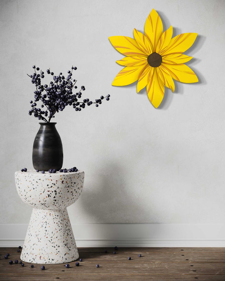 Handcrafted curled top petal flower decor in yellow on white wall above a terrazzo table with a black vase.