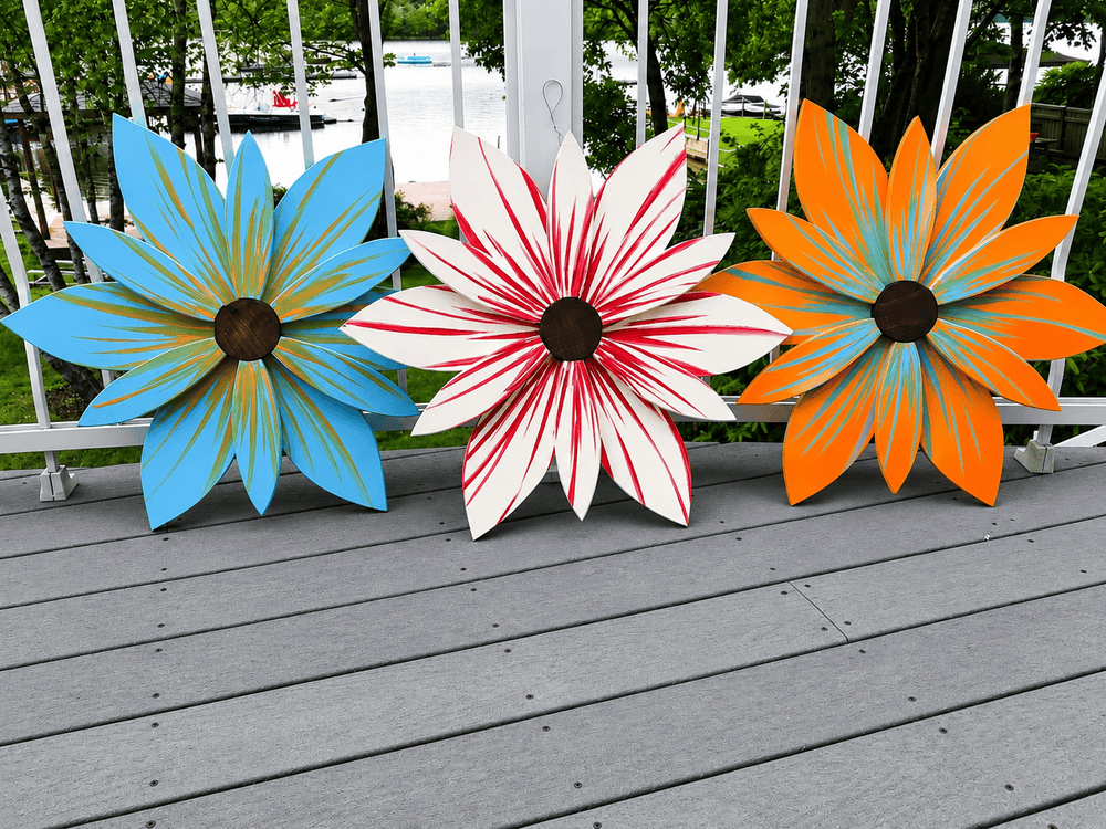 Three colorful metal flower sculptures on a wooden deck with a blurred outdoor background.