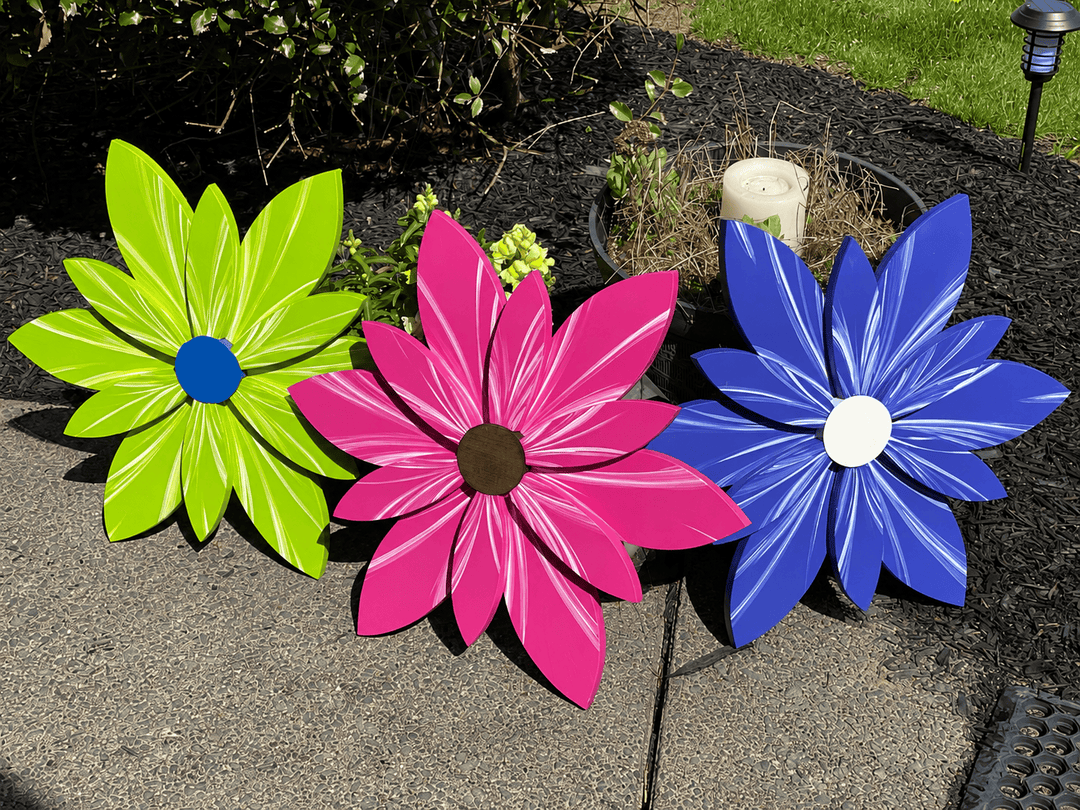 Three colorful flower-shaped decorations on a pavement with a garden background.
