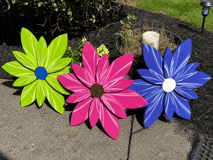 Three colorful flower-shaped decorations on a pavement with a garden background.