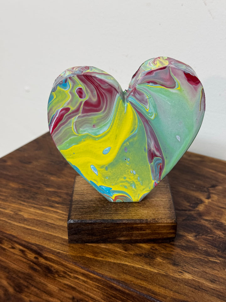 Colorful heart-shaped object on a wooden stand against a white background