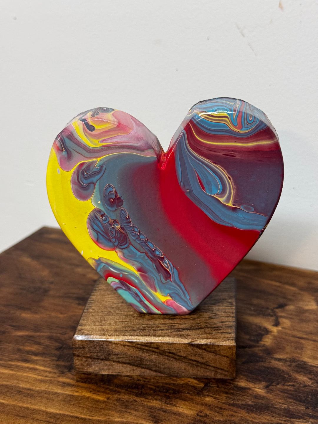 Colorful heart-shaped object on a wooden stand against a white background