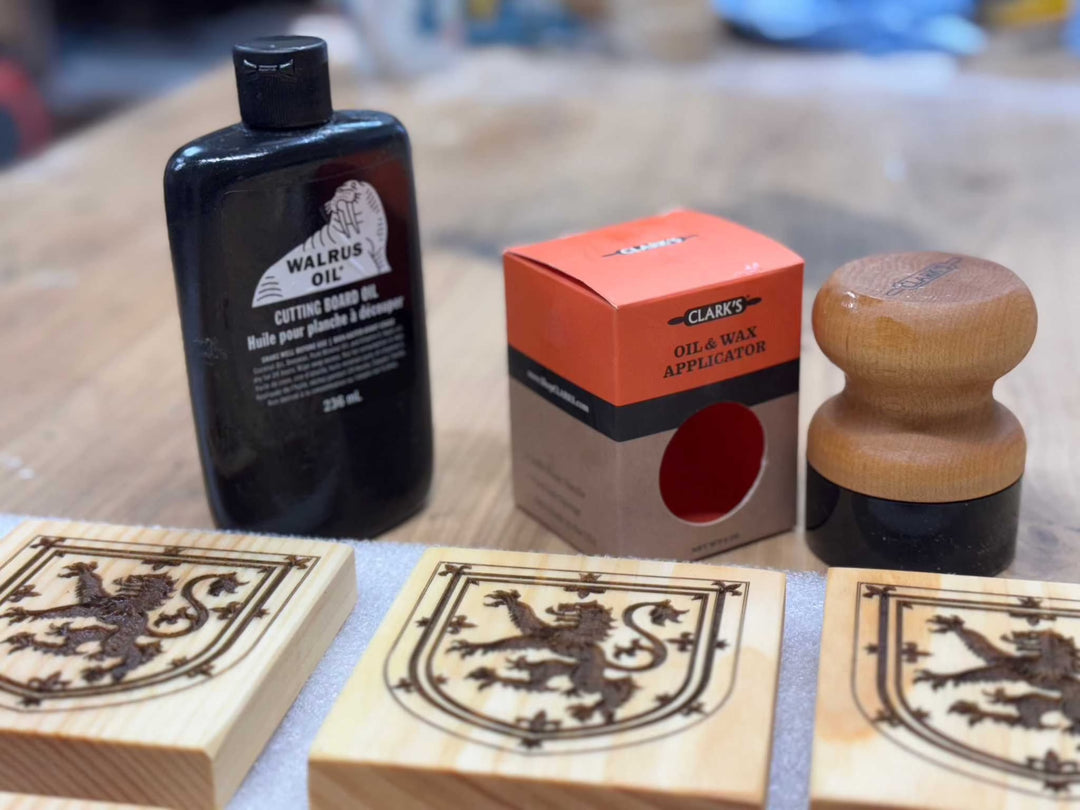 Handcrafted Nova Scotia wood coasters with engraved Coat of Arms and finish options like Walrus Oil, alongside oil and wax applicator on a table.