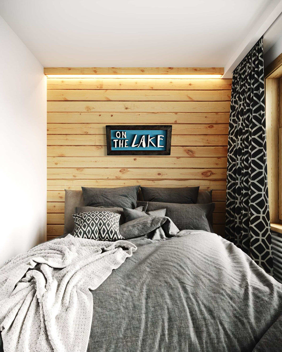 Handcrafted wooden sign with "On The Lake" hand-drawn letters, displayed on a pine wall above a bed.