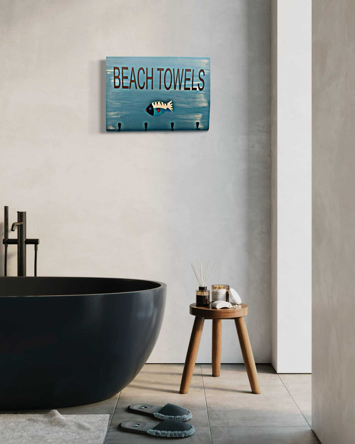 Hand-painted wooden fish hook beach towel holders with ocean-themed design, mounted above a modern black bathtub.