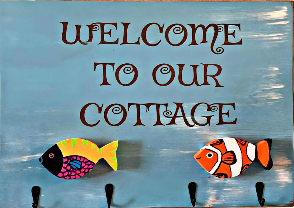 Laser engraved wood folk art sign with "Welcome to Our Cottage" text, fish motifs, and hooks.