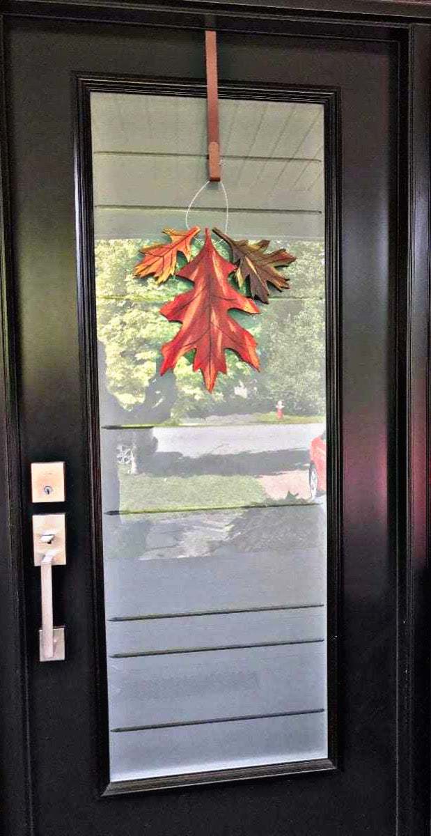 Handmade painted oak leaf decor hanging on a black door, crafted from pine wood in Canada.