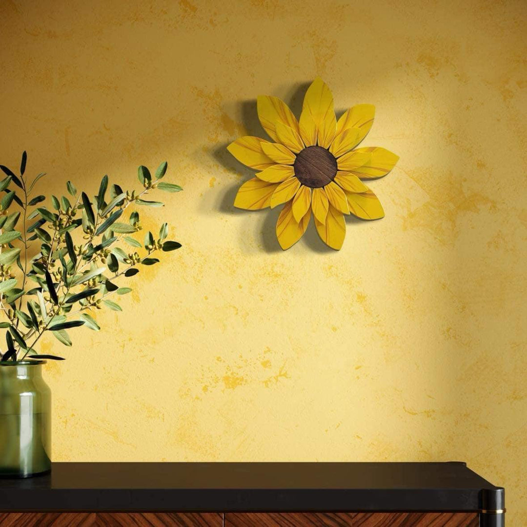 Handcrafted wooden sunflower decoration on yellow wall near vase.