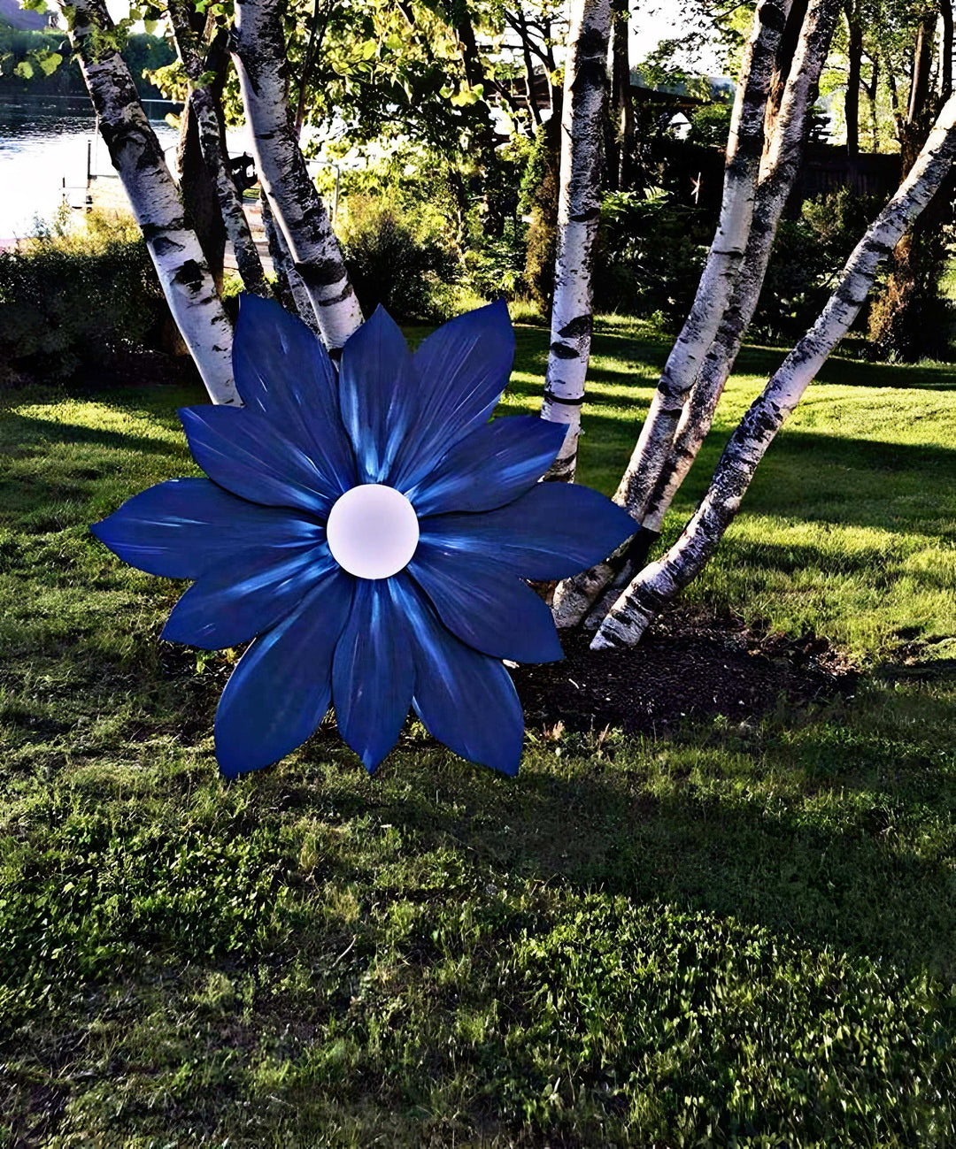 Giant wooden flower decoration in vivid blue, handcrafted with pine wood, outdoors in a garden setting.