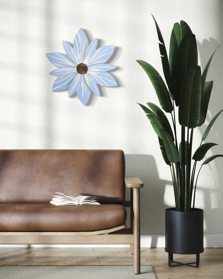 Costa Rica Blue Wood Flower Door Decoration displayed on a wall above a brown sofa, next to a tall potted plant.