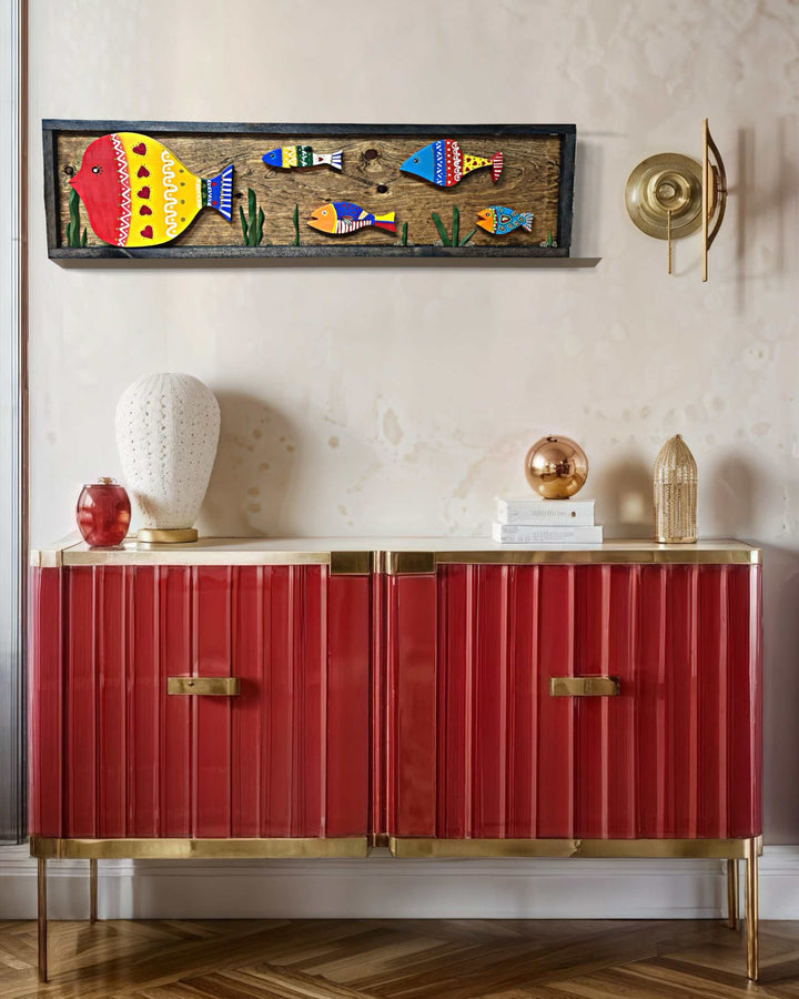 Handmade wooden fish wall art with vibrant colors above a red cabinet in elegant home setting.