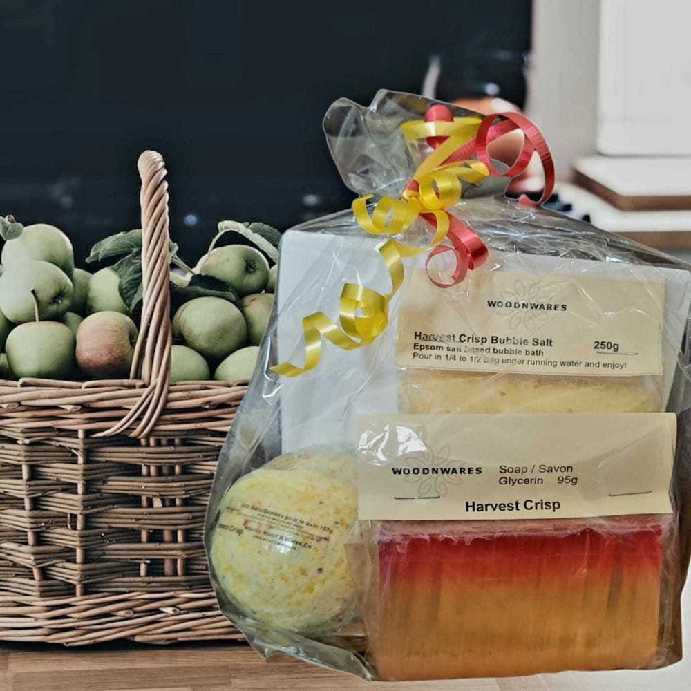 Luxurious gift set includes handmade soap, bath bomb, and bubble bath Epsom salt, wrapped with festive ribbon, placed next to a basket of apples.