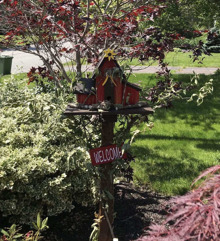 Triple birdhouse in a garden setting with welcome sign, crafted from pine wood, featuring three compartments, customizable for bird enthusiasts.