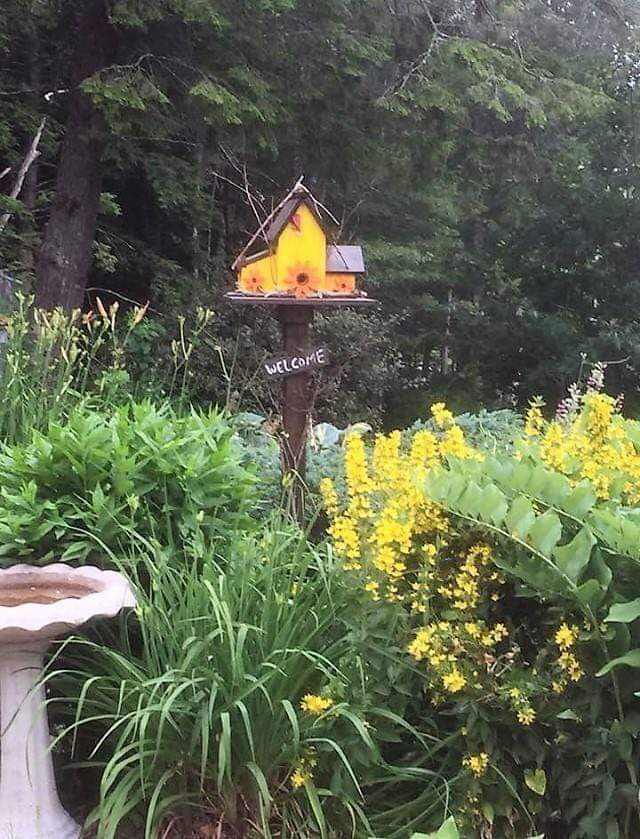 Triple birdhouse in garden setting with vibrant flowers and greenery.