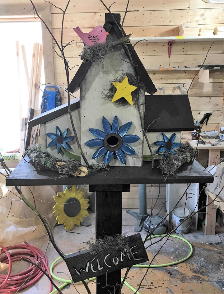 Triple birdhouse with blue flower accents, yellow star decoration, pink bird figurine, and "Welcome" sign for garden decor