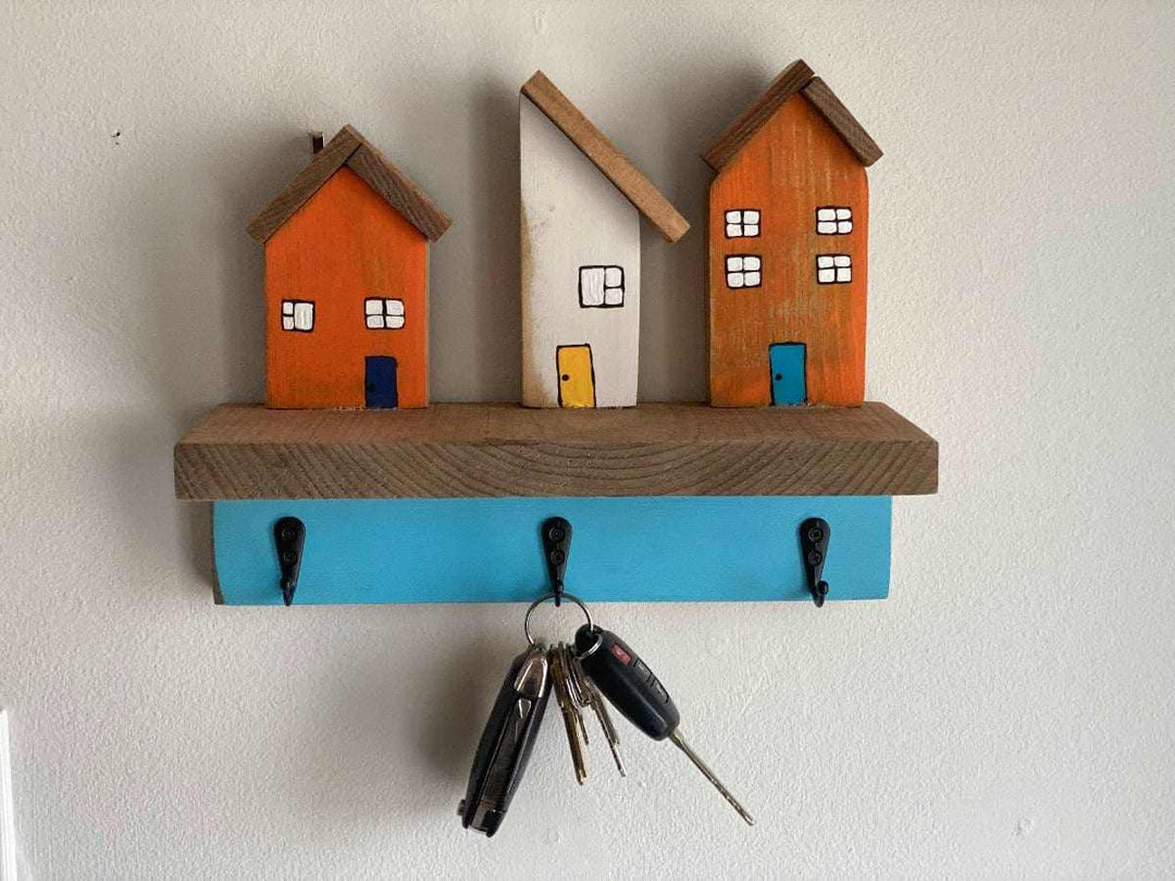 Wall mounted key chain holder with three colorful house designs and hooks.