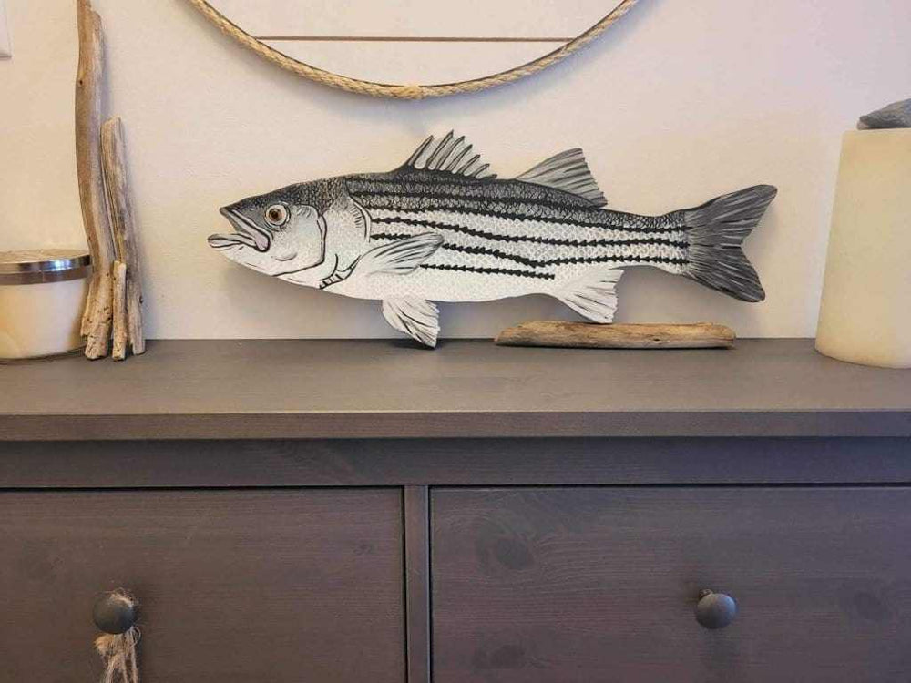 Hand-painted striped bass artwork on a dark wooden shelf with coastal decor elements.