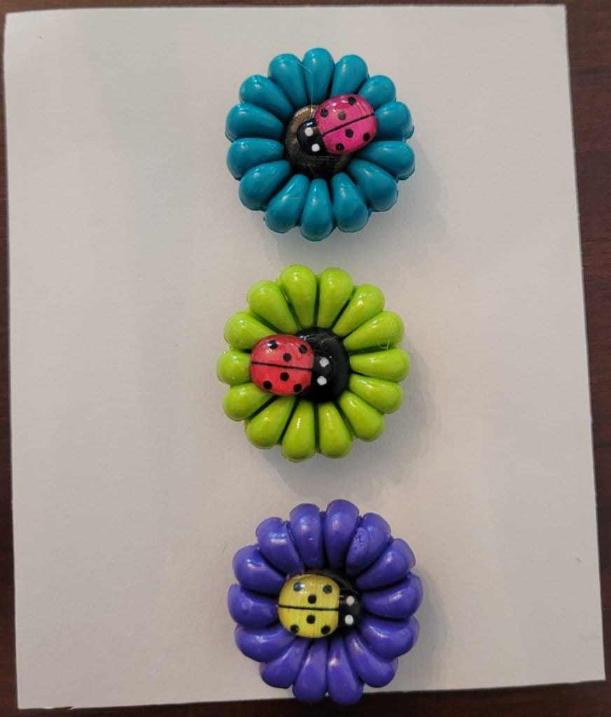 Polymer clay fridge magnet set with daisy flowers and ladybugs in blue, green, and purple.