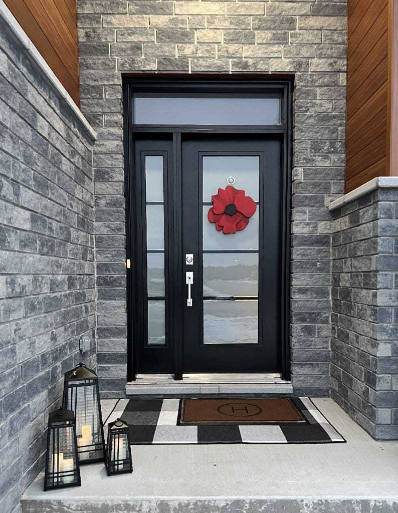 Handcrafted wooden anemone-inspired door decor in vivid red with striking black center displayed on a modern front door.