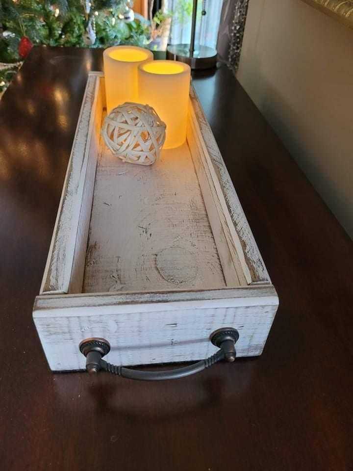 Antiqued wooden trays with handles and candles on a dark tabletop.