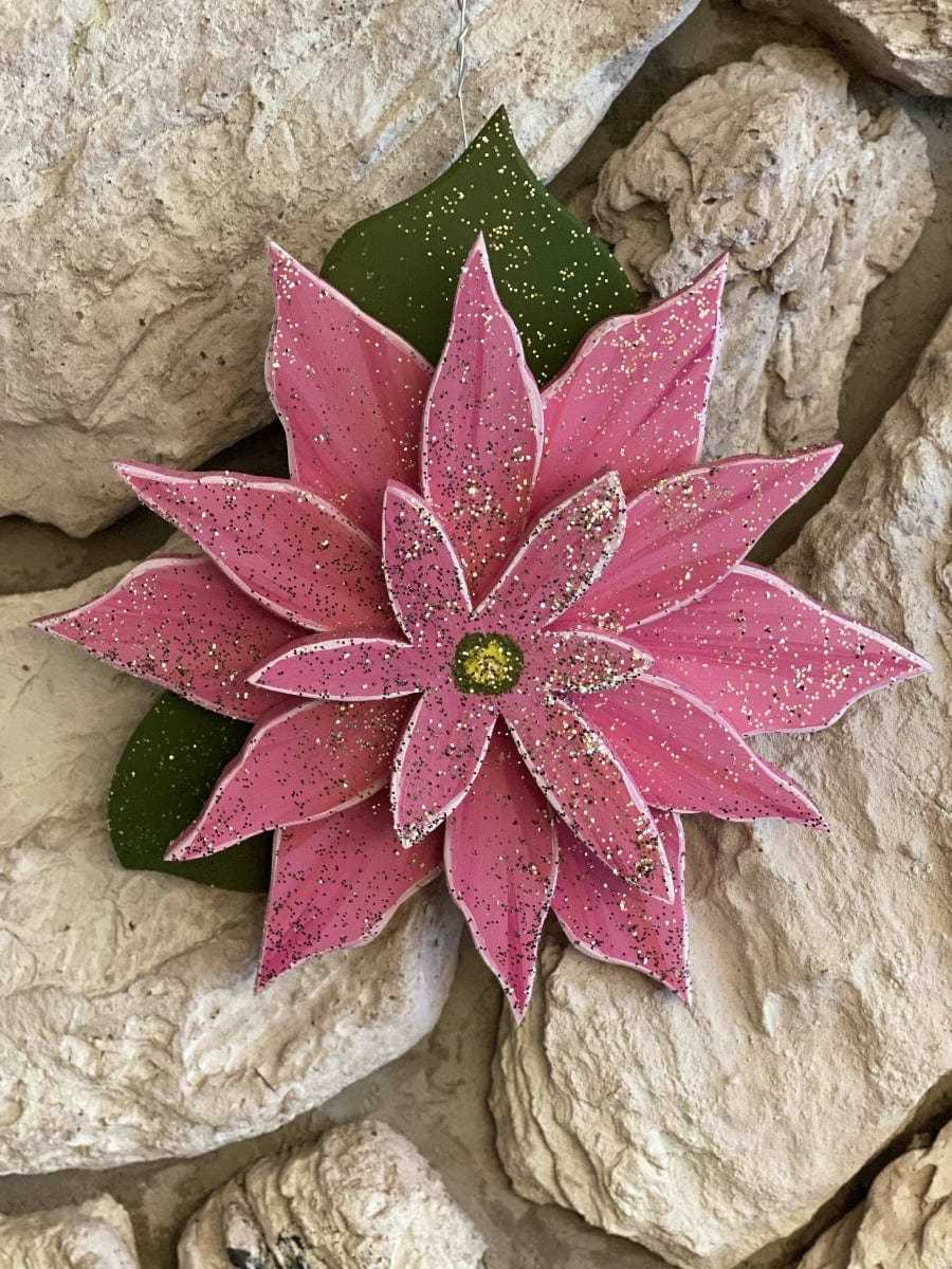 Wooden pink poinsettia decoration on rocks, symbolizing joy and celebration for the holiday season.