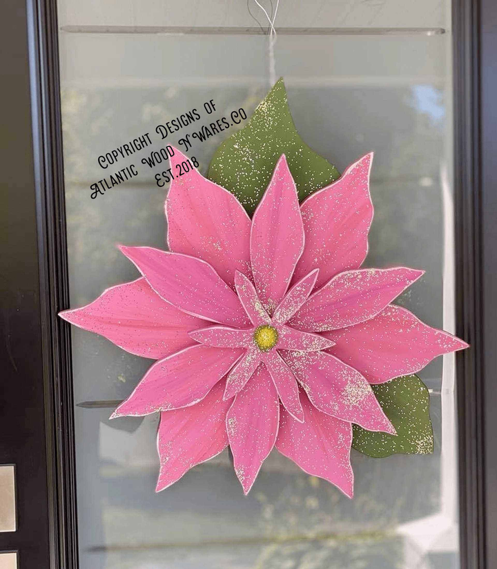 Wooden Poinsettia flower decoration with pink petals, green leaves, and a wire hanger, symbolizing Christmas spirit and joy.