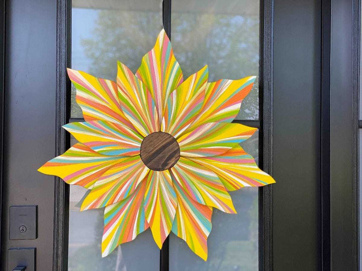 Colorful handcrafted wooden flower door decoration with striped petals and wooden center hanging on black door