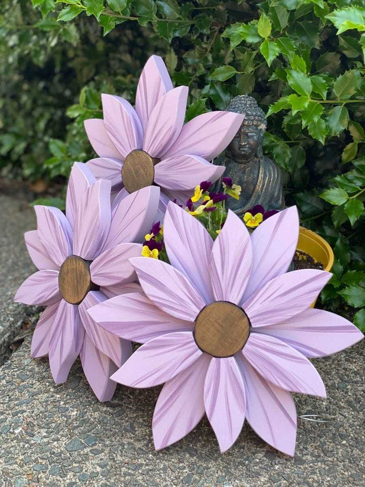 Elegant wooden flower art pieces in lavender, set in a garden with lush greenery.