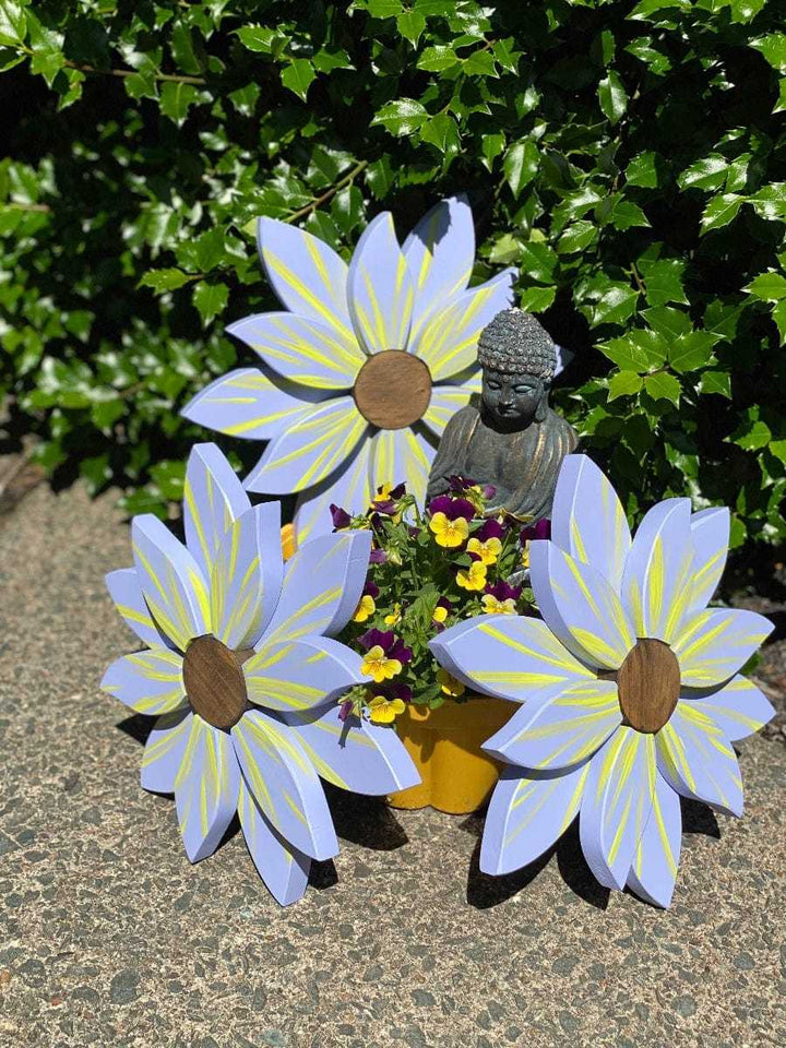 Wooden flower art pieces with vibrant petals and stained wooden centers, displayed outdoors with a small Buddha statue and flowers.
