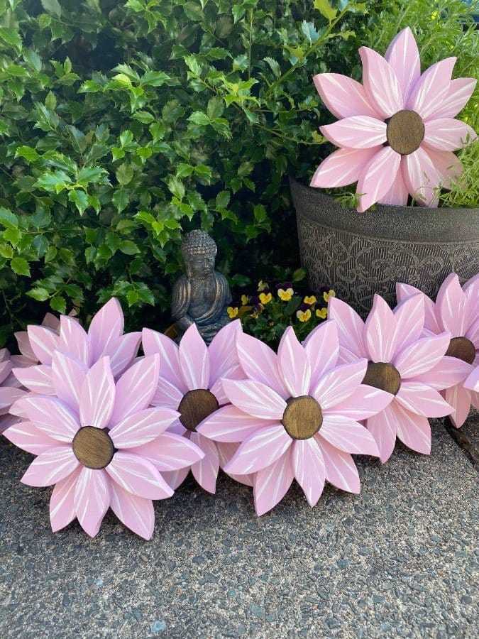 Elegant wooden flower art pieces displayed outdoors with pink petals and stained wooden centers, enhancing garden charm.