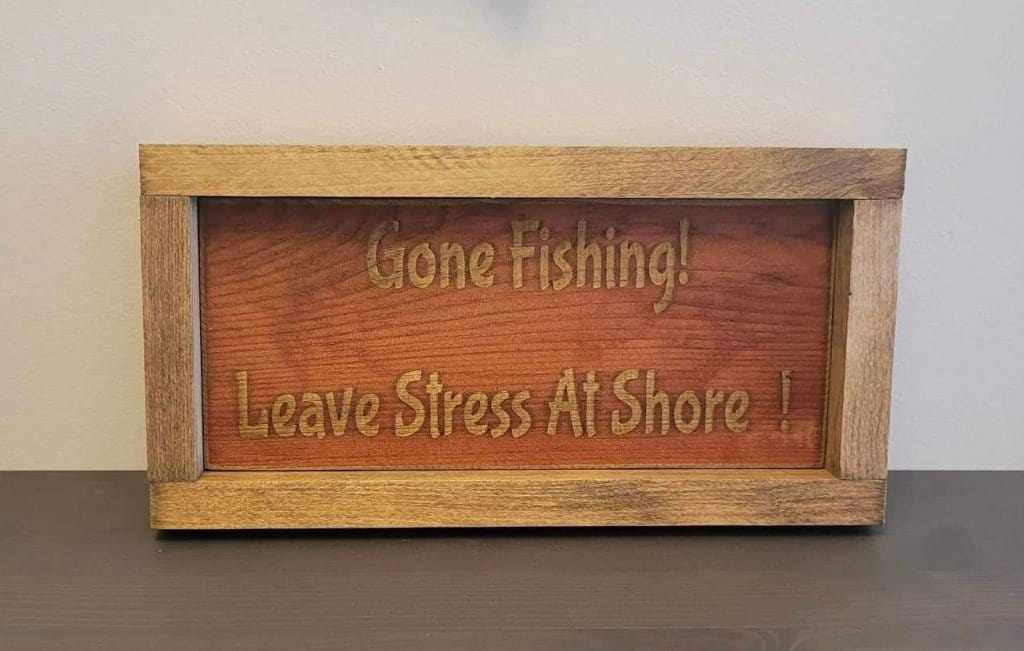 Laser engraved wood sign with "Gone Fishing! Leave Stress At Shore!" message, perfect for outdoor enthusiasts.