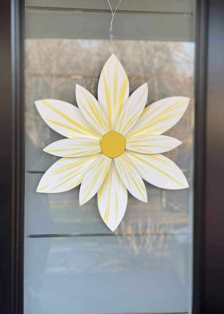 Handcrafted sunburst flower wood art with white and yellow petals, hanging on a door.