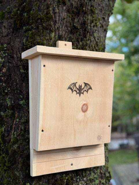 Handcrafted pine bat house with laser-engraved bat design, mounted on a tree for easy installation and wildlife conservation.