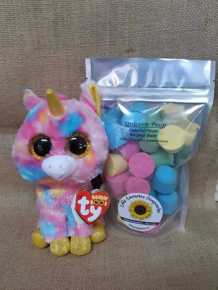 Colorful unicorn plush toy beside a pouch of Unicorn Poop bath bombs with vibrant pastel colors for fun, foaming baths
