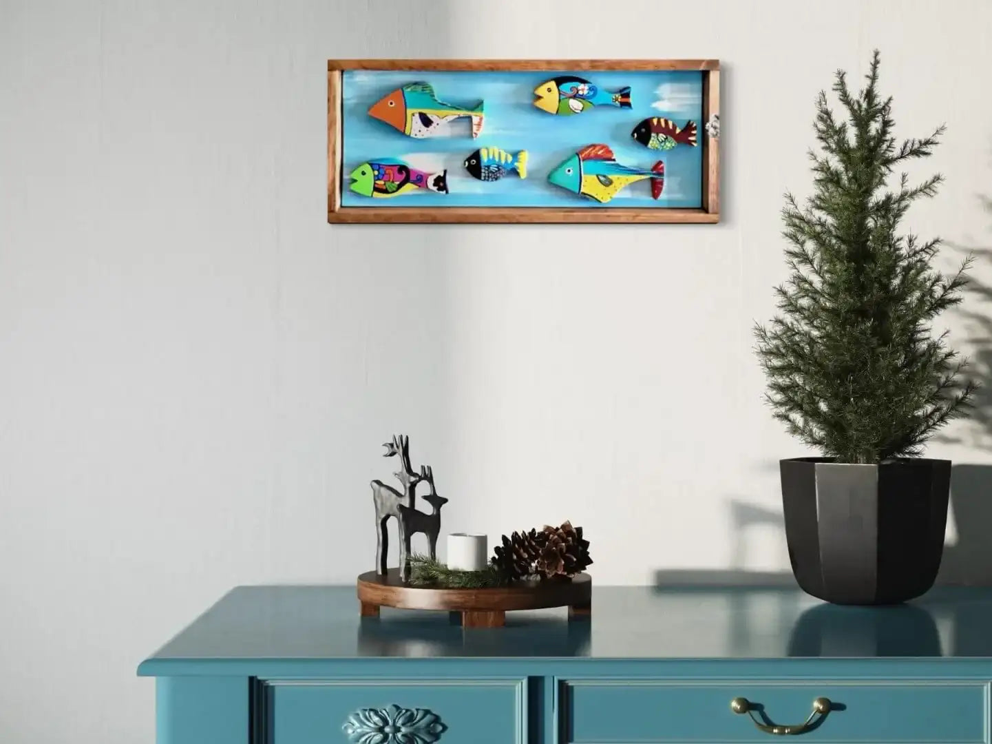 Blue wooden dresser with decorative items on top, including a deer figurine and potted plant.assistant: colorful fish-themed wall art in an oak frame hanging above the dresser.