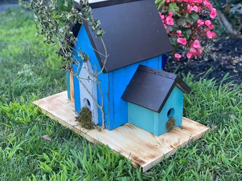 Triple birdhouse on a wooden base with vibrant blue paint in a garden setting.