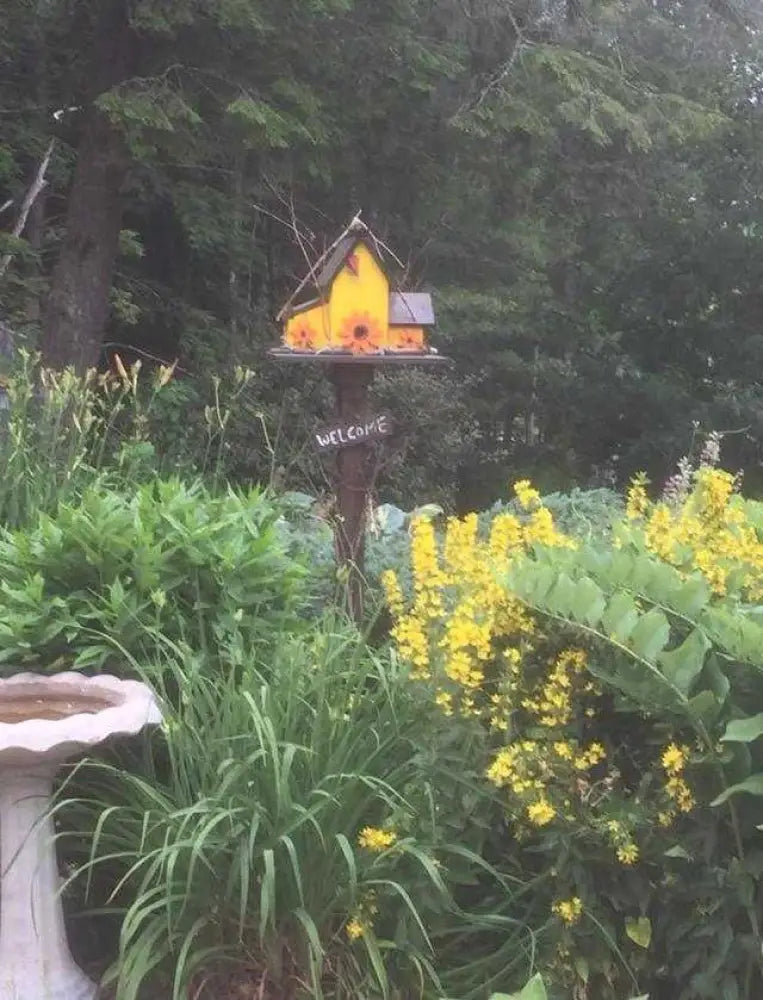Triple birdhouse garden decoration with yellow birdhouse and welcome sign surrounded by green plants and yellow flowers