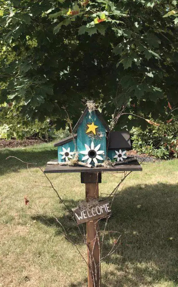 Triple birdhouse with three compartments, perched on a stand, featuring custom colors and designs in a garden setting.