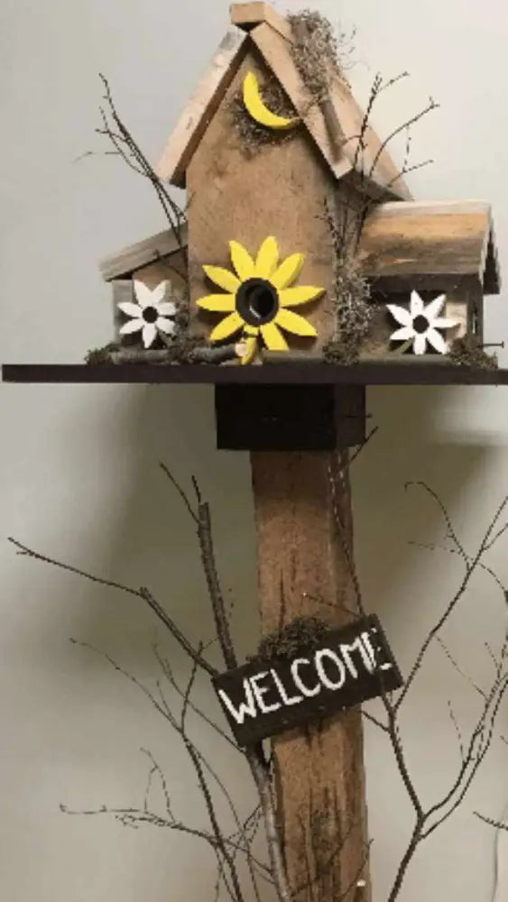 Triple wooden birdhouse with sunflower and moon decorations and welcome sign on wooden pole