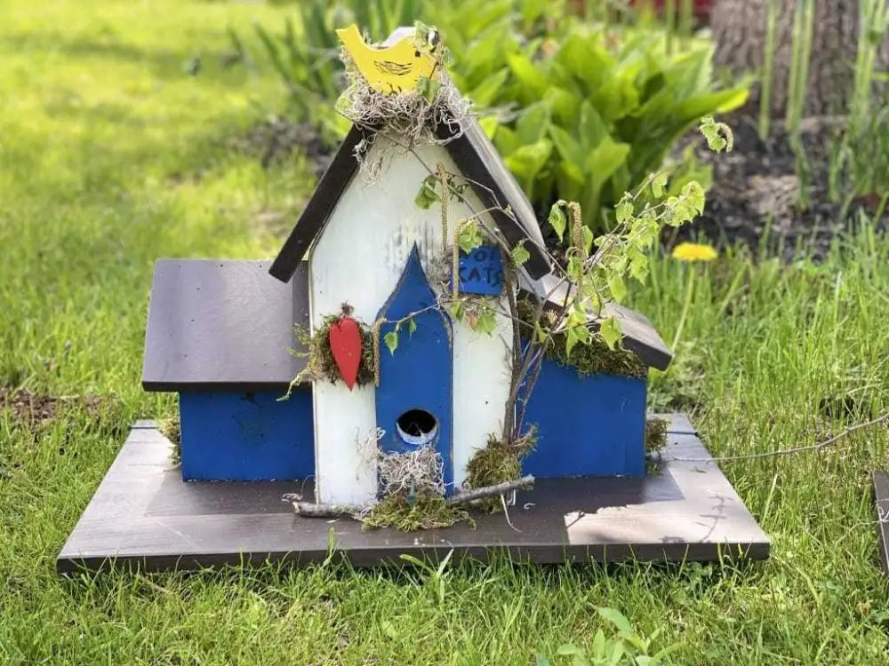 Blue and white triple birdhouse with personalized decoration in a garden setting.