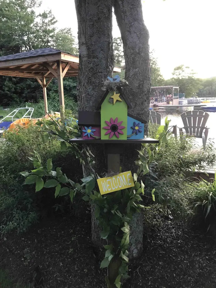 Triple birdhouse on tree with colorful floral accents in garden setting.