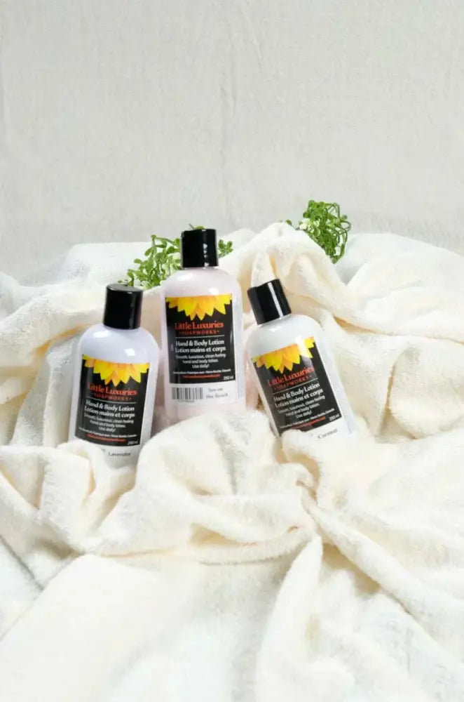 Three bottles of Coconut Oil Hand and Body Lotion on a soft white towel with green plant accents