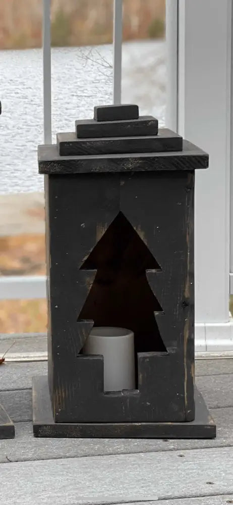 Handcrafted wooden lantern with tree cutout design on a porch.
