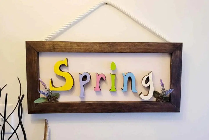 Handmade wooden sign with colorful "Spring" letters and rope for hanging.